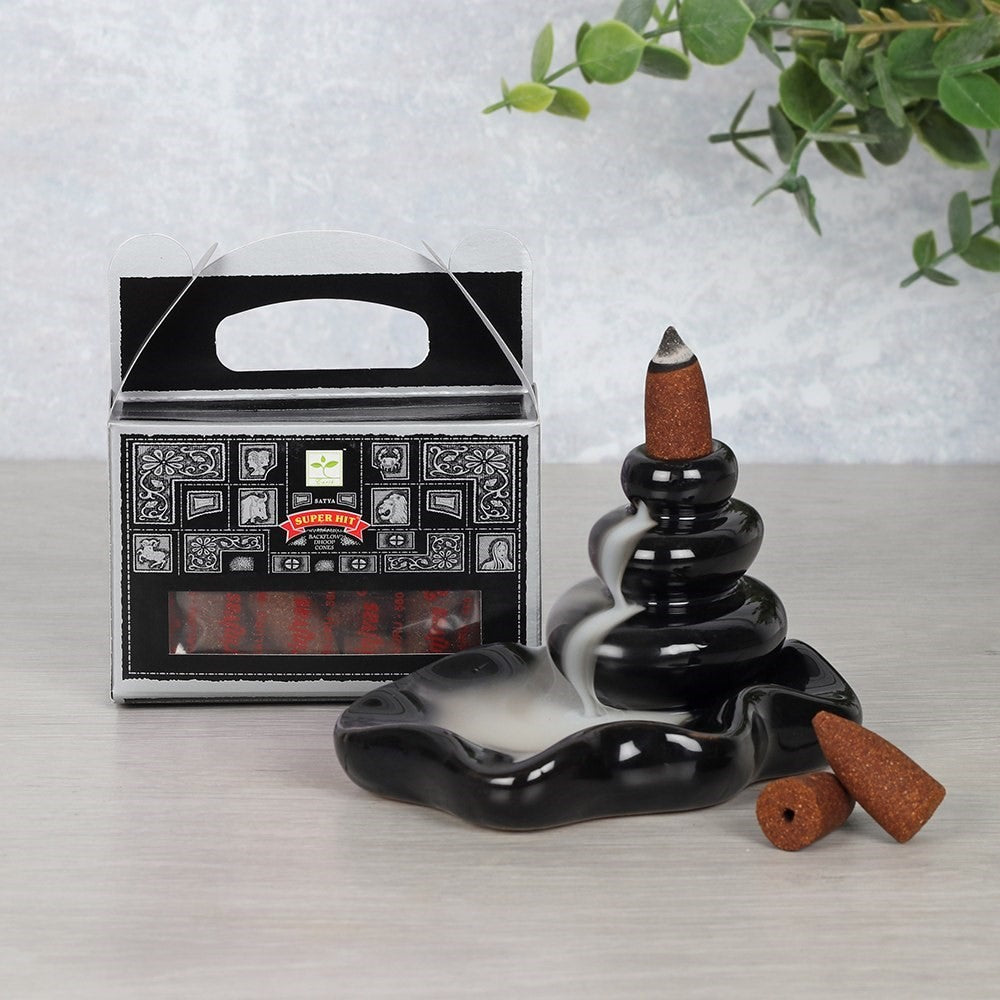Black incense burner with cones and packaging on a light surface with greenery.