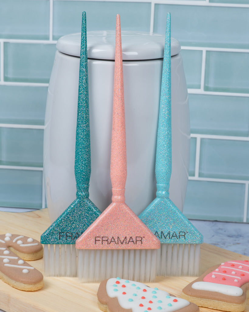 Three glittery brooms with 'Framar' branding on a kitchen counter with cookies.