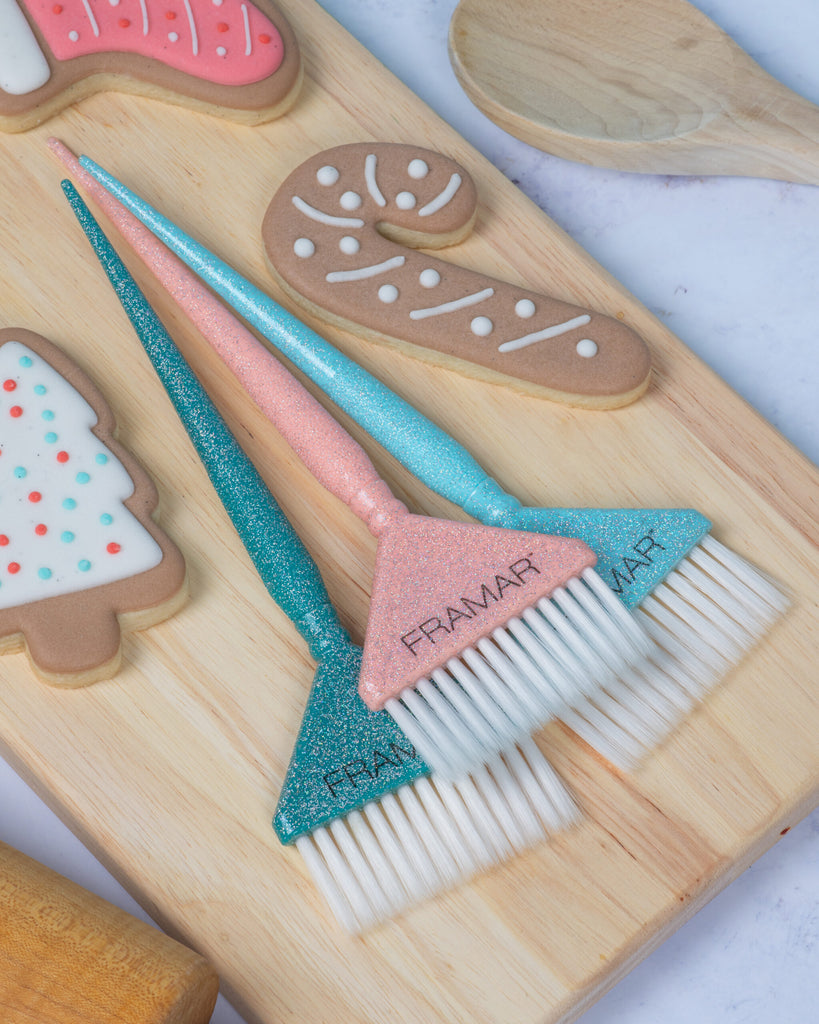 Two decorative brushes with glittery handles on a wooden board with gingerbread-themed cookies.