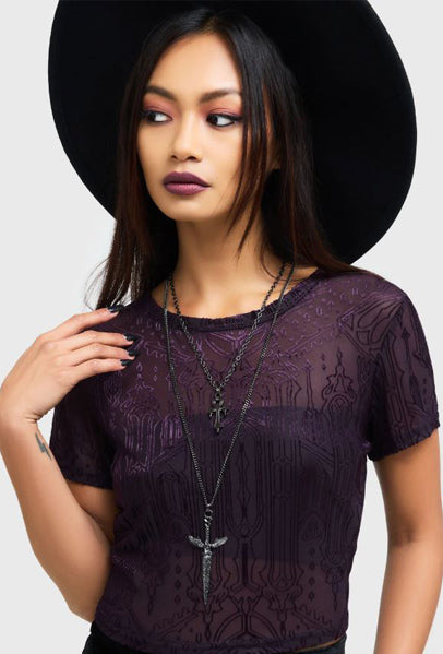 Woman wearing a dark purple lace top and black hat on a white background
