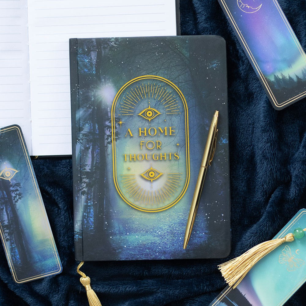 Notebook with 'A Home for Thoughts' design, pen, and phone on a dark fabric background