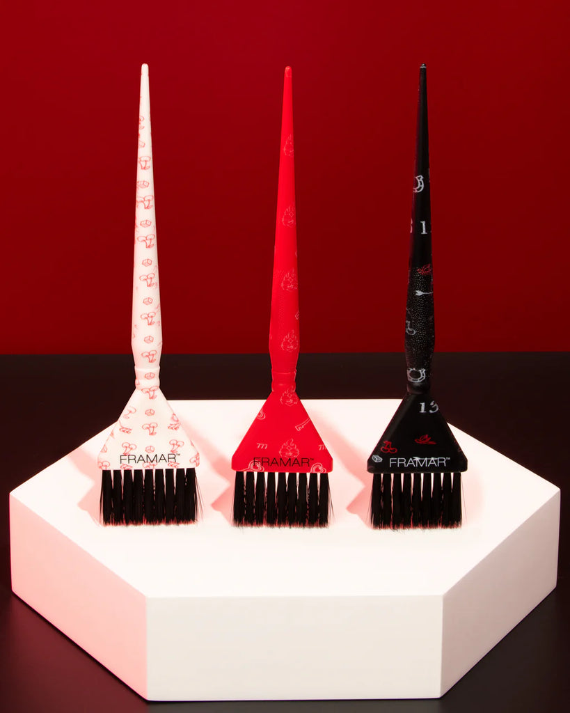 Three hair dye brushes with color guides on a white stand against a red background