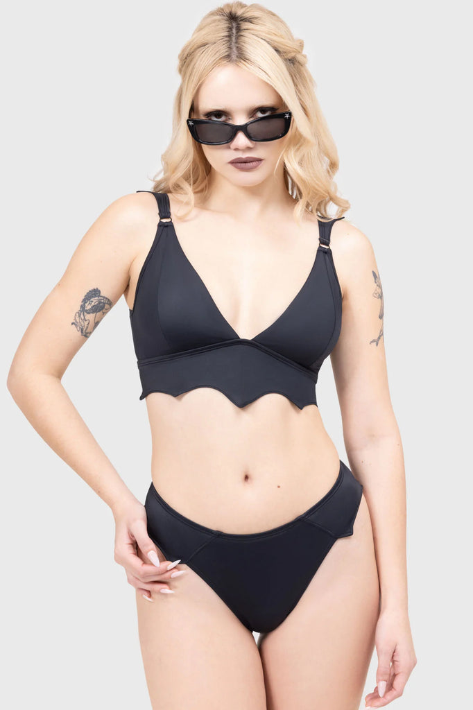 Woman wearing a black bikini and sunglasses on a plain background