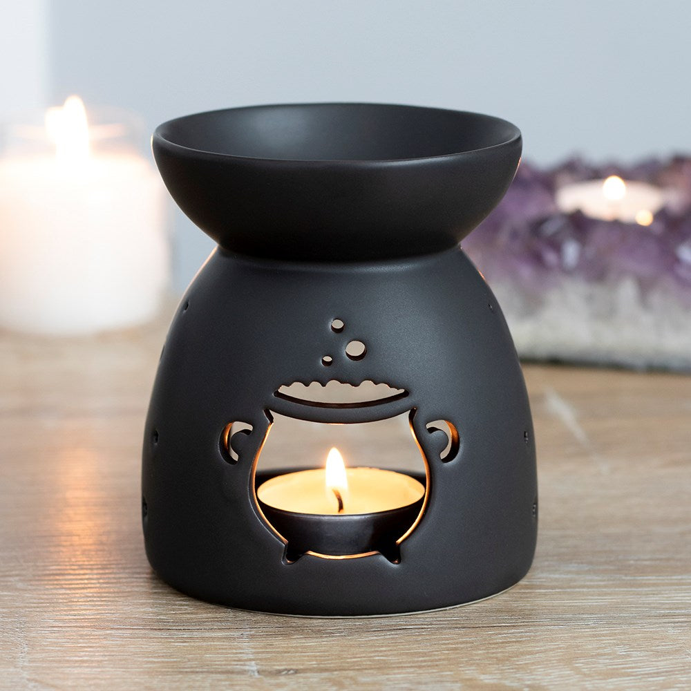 Black ceramic oil burner with a lit candle inside on a wooden surface.