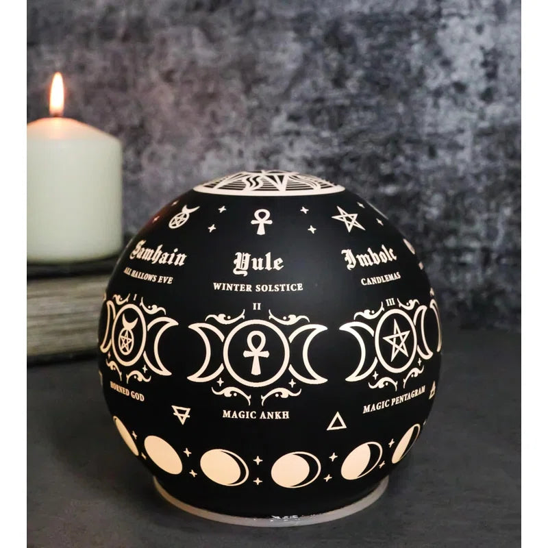 Black decorative orb with white symbols and text, placed on a dark surface with a candle in the background.