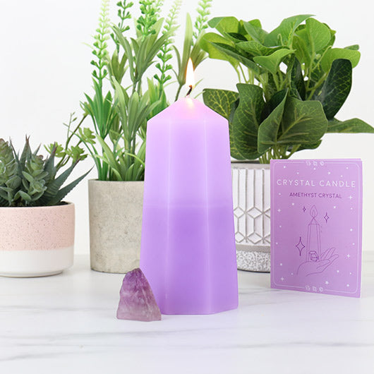 Purple candle with packaging, amethyst crystal, and plants on a white surface