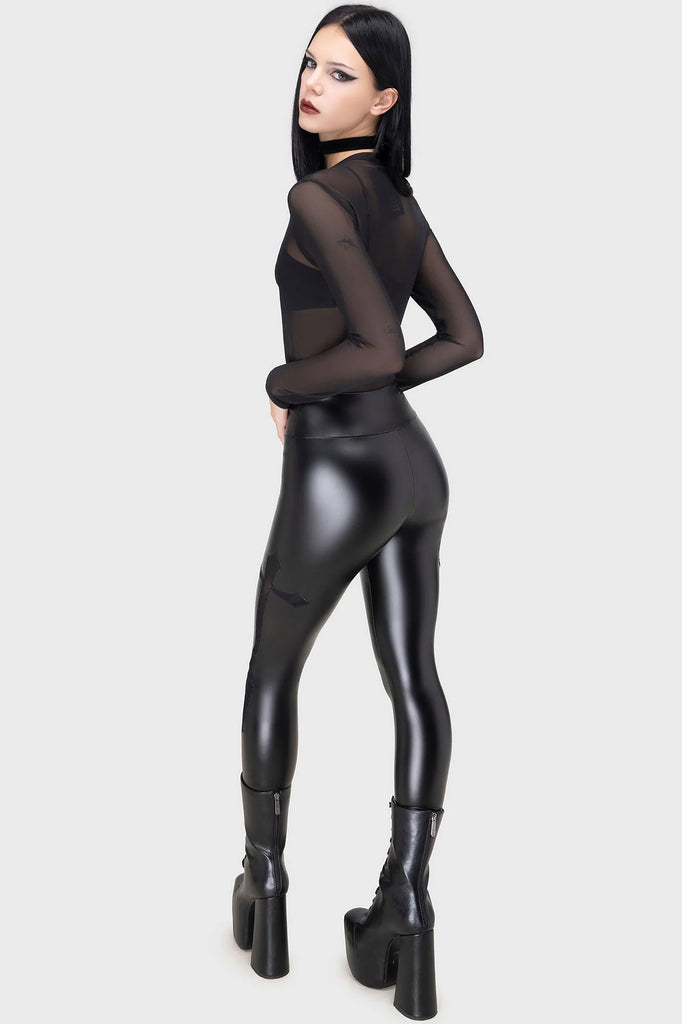 Person wearing a black sheer top and shiny black pants on a white background