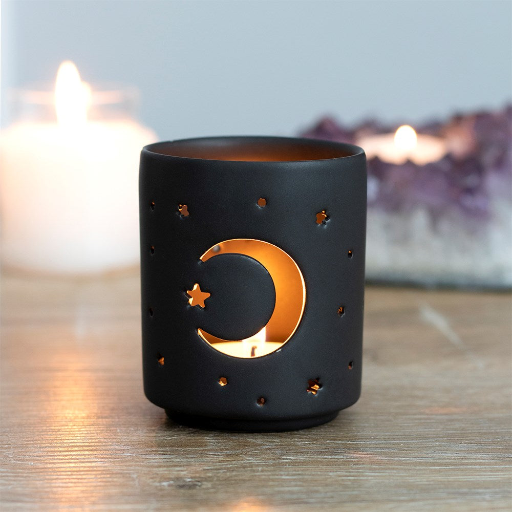 Black candle holder with moon and star design on a wooden surface with candles in the background.