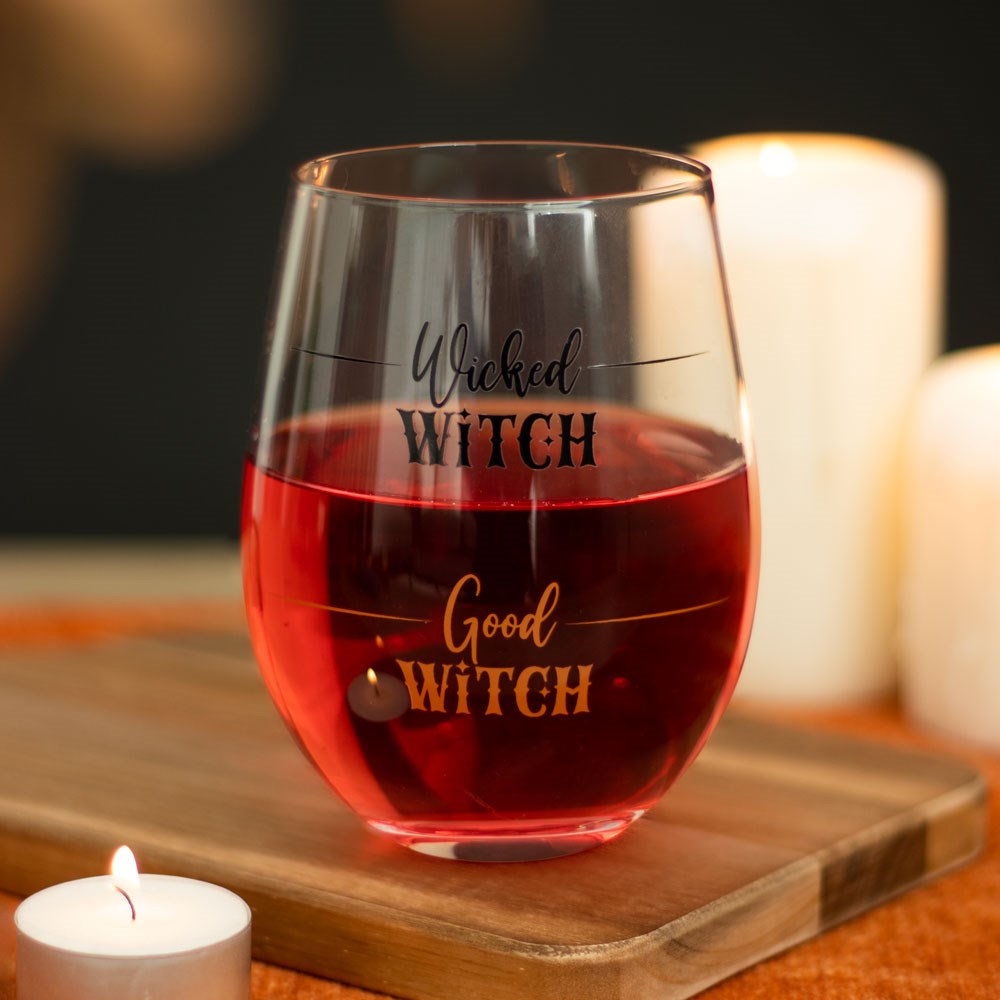 Wine glass with 'Wicked Witch, Good Witch' text on a wooden board with candles in the background.