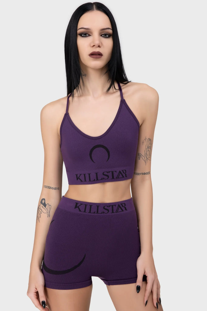 Woman wearing a purple 'Killstar' sports bra and shorts on a white background