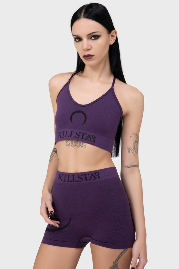 Woman wearing a purple 'Killstar' sports bra and shorts set on a white background