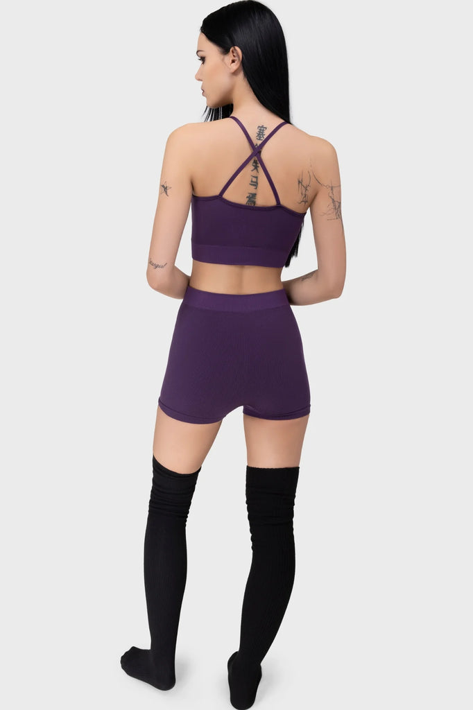 Person wearing a purple sports bra and shorts set with black knee-high socks on a white background