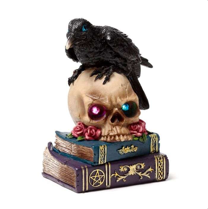 Decorative skull with colorful eyes, black crow, and books on a white background