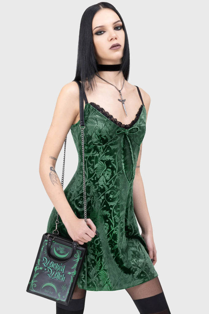 Woman wearing a green velvet dress holding a black handbag with green text.