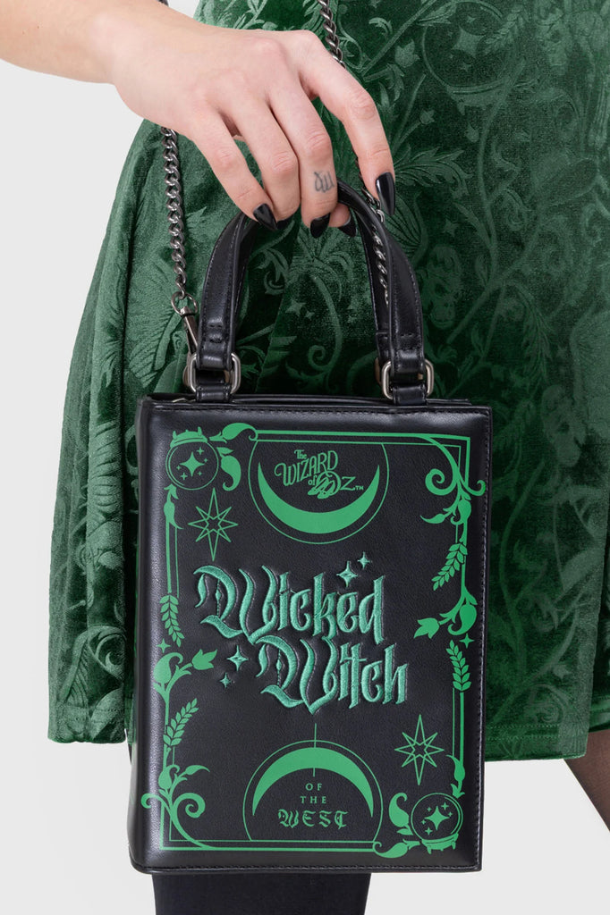 Black handbag with 'Wicked Witch' design held by a person wearing a green dress.