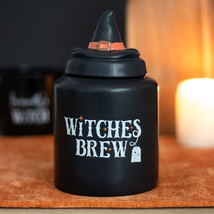 Black container with witch hat lid labeled 'Witches Brew' on an orange surface.