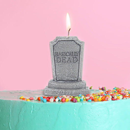 Graveyard tombstone candle with 'Basically Dead' text on a cake against a pink background
