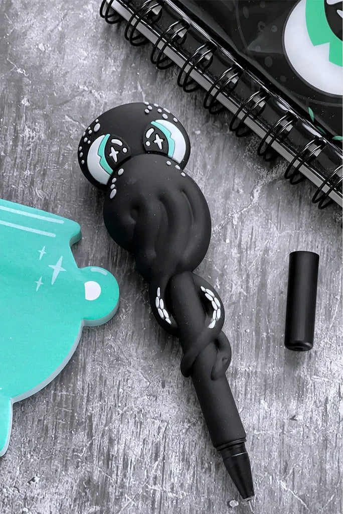Black silicone straw with a design on a gray surface next to a teal puzzle piece and a black notebook.