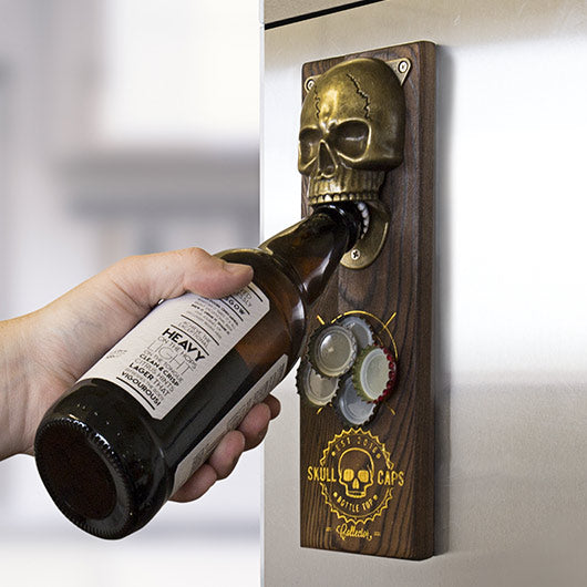 Skull-shaped bottle opener mounted on a wall with a hand holding a bottle.
