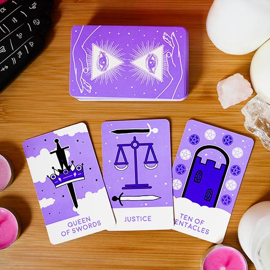 Purple tarot cards with illustrations on a wooden surface with crystals and candles.
